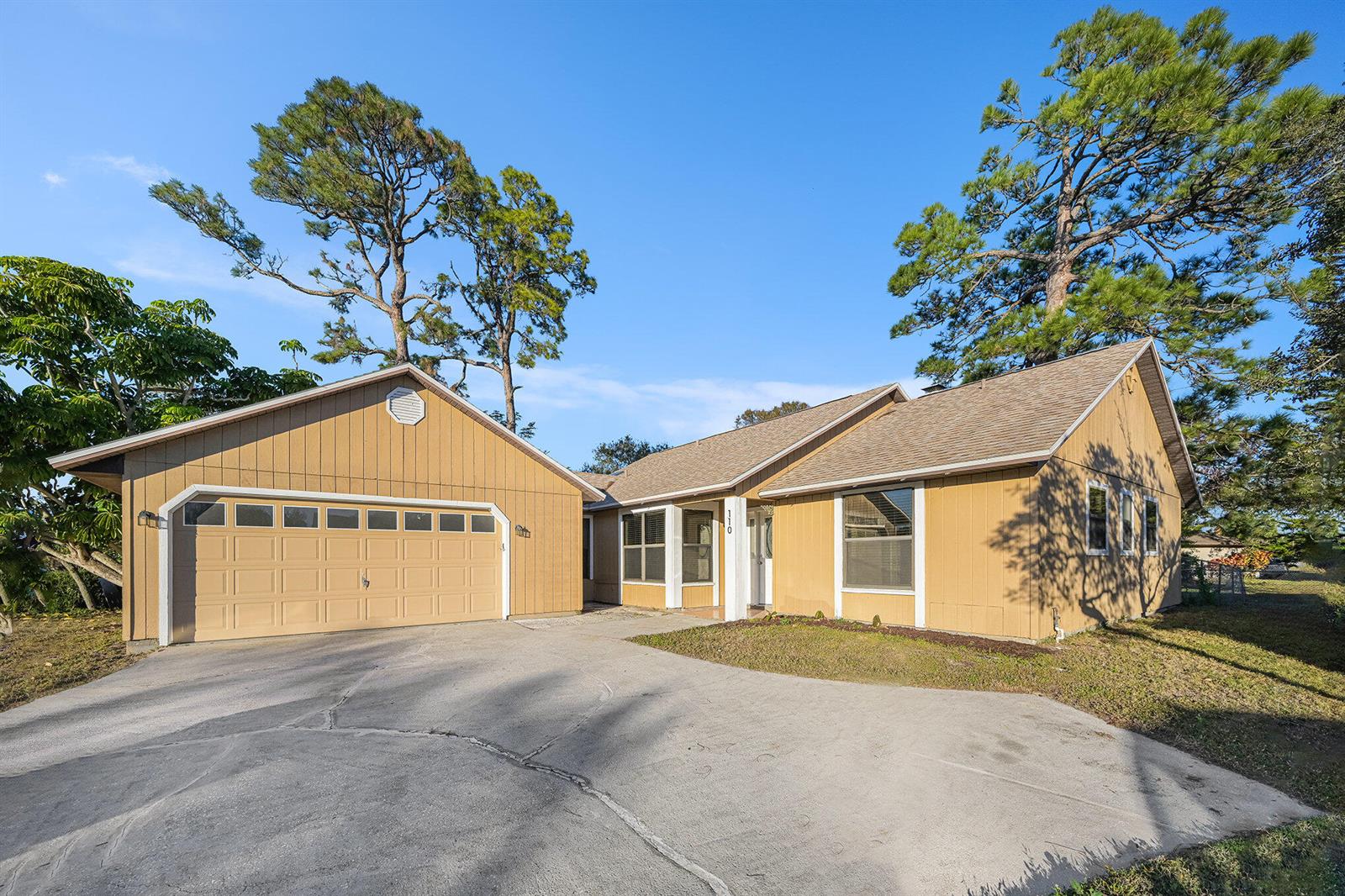 A tan, single-story house with a two-car garage and a concrete driveway under blue skies — 110 Cardinal Drive, Sebastian FL 32958, SEBASTIAN, FL