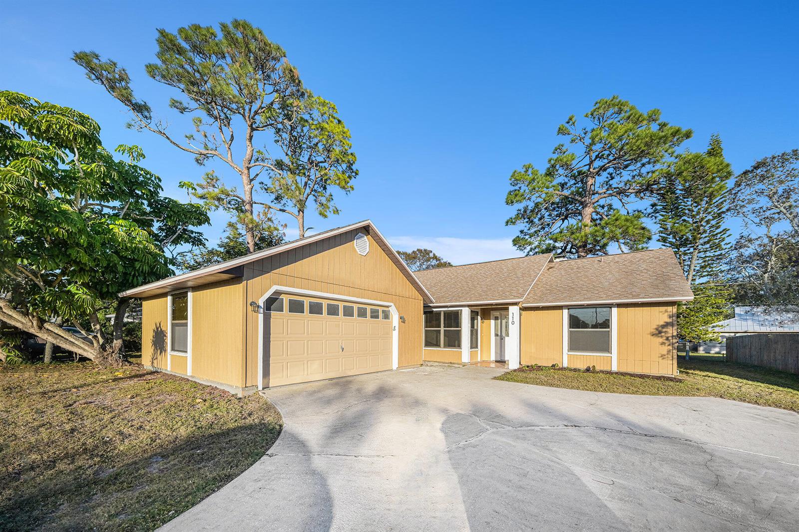 A single-story house with tan vertical siding, a two-car garage, and a concrete driveway — 110 Cardinal Drive, Sebastian FL 32958, SEBASTIAN, FL