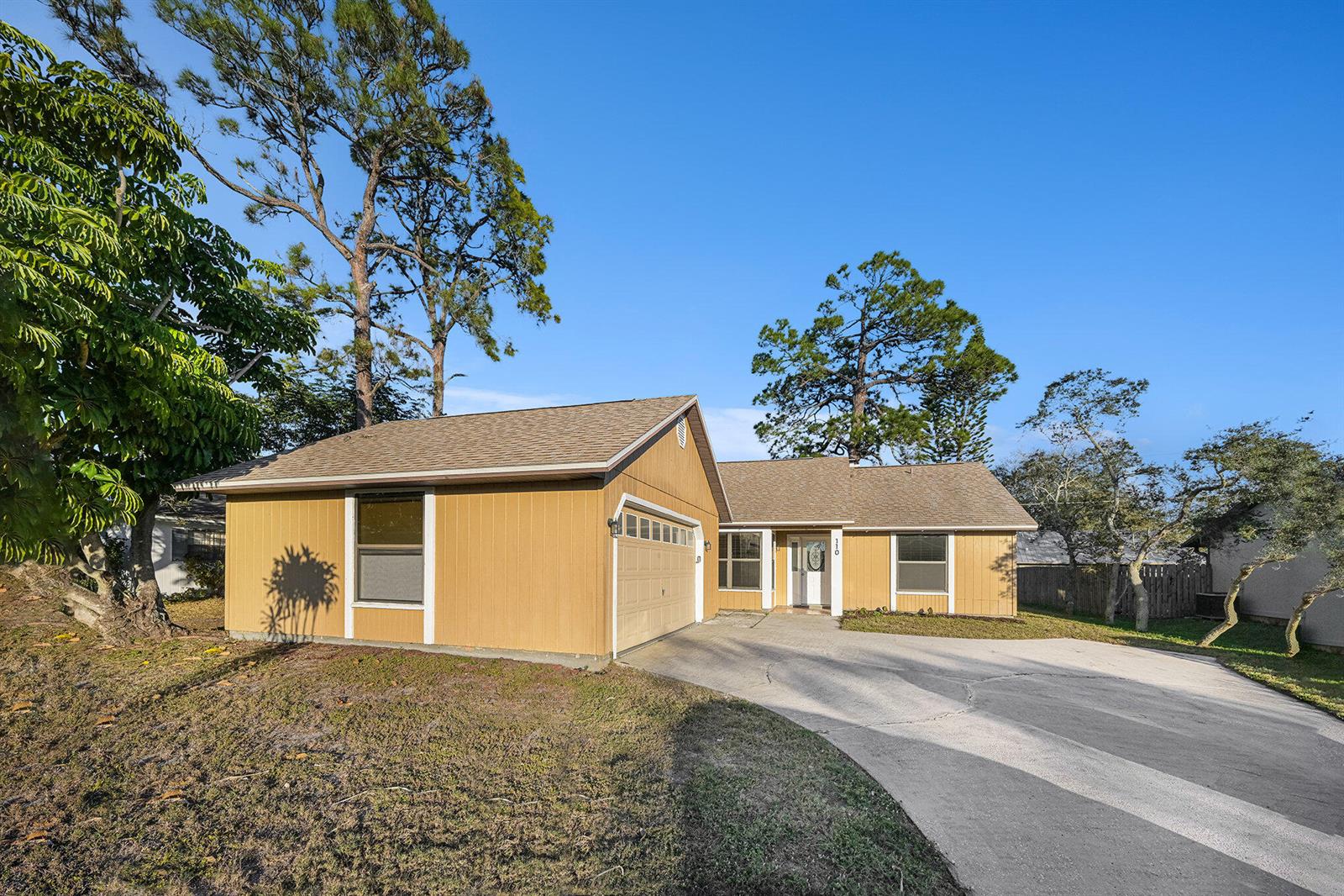 A single-story house with yellow siding, a garage, and a concrete driveway under blue skies — 110 Cardinal Drive, Sebastian FL 32958, SEBASTIAN, FL