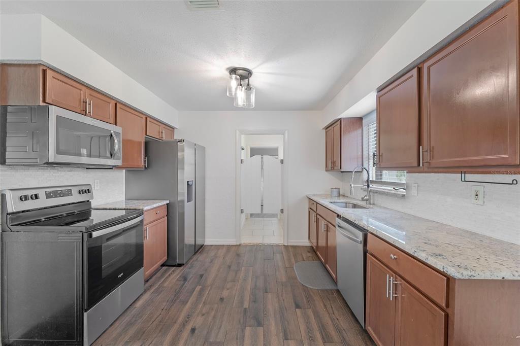 A kitchen features wood cabinets, stainless steel appliances, granite countertops, and wood-look flooring — 20310 LORENZO AVENUE, PORT CHARLOTTE, FL