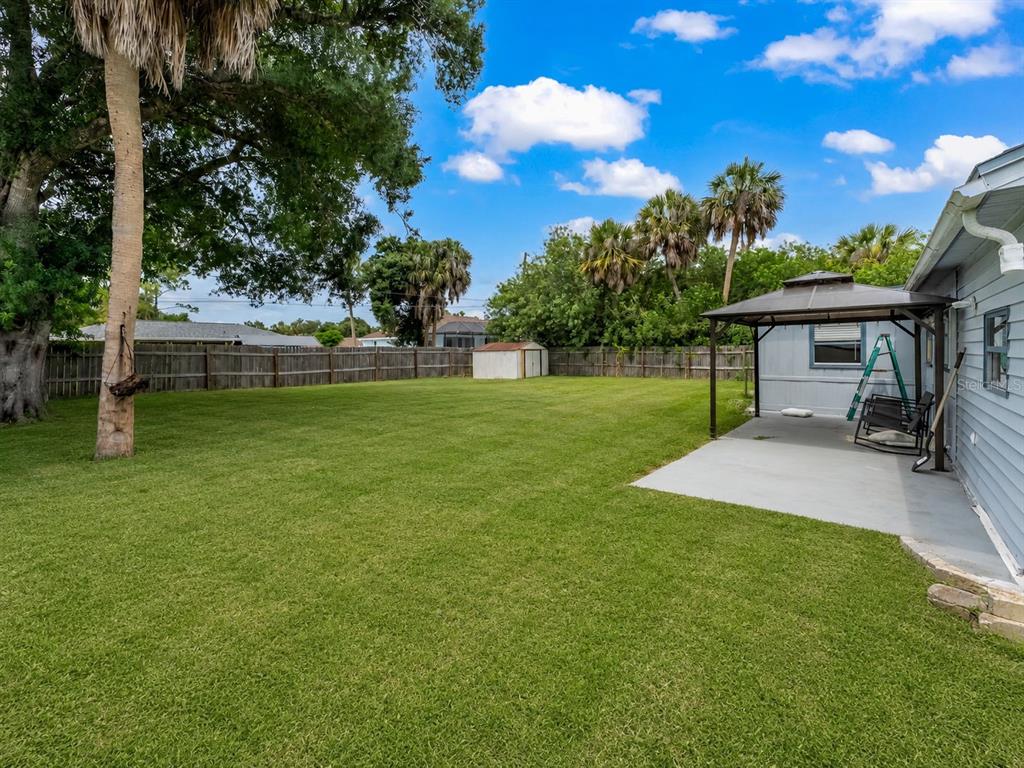 A grassy backyard features a concrete patio, a metal gazebo, and a wooden fence — 20310 LORENZO AVENUE, PORT CHARLOTTE, FL