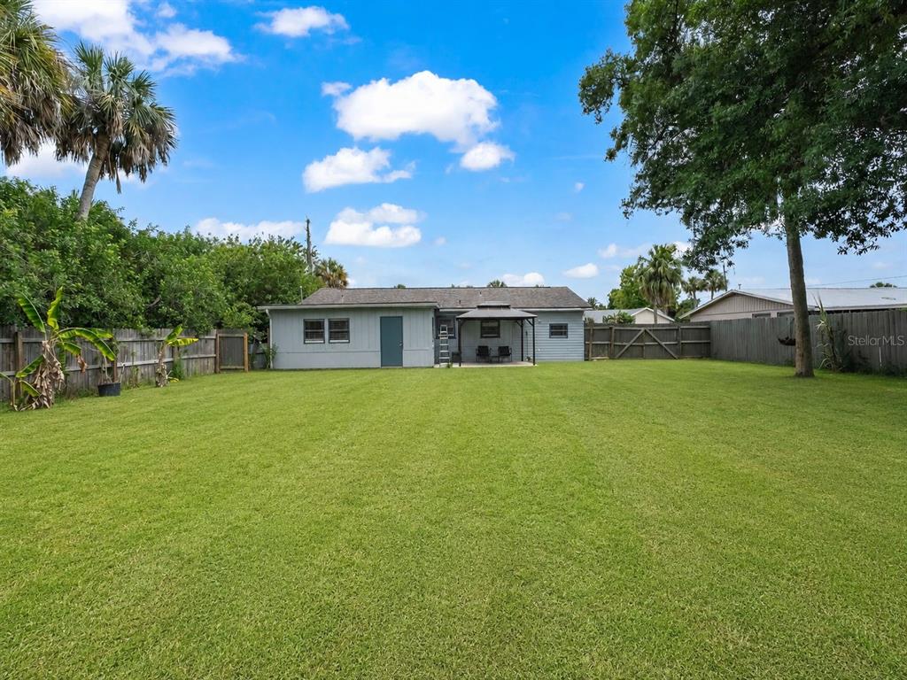 A backyard with a large lawn, a gray house, and a wooden fence — 20310 LORENZO AVENUE, PORT CHARLOTTE, FL
