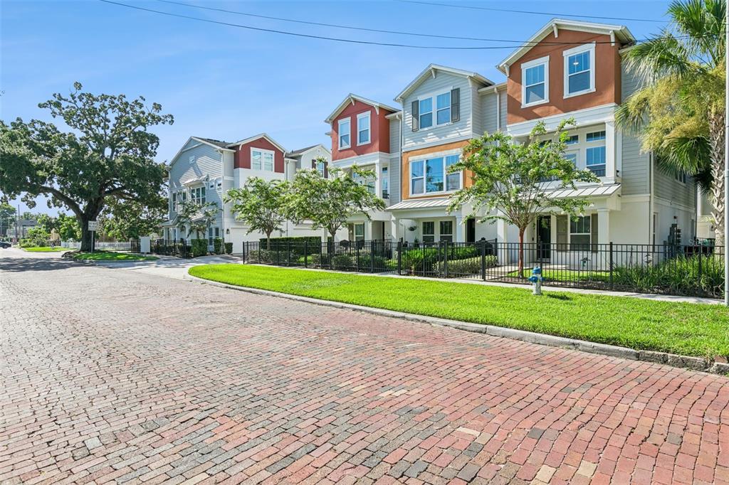 A row of three-story townhomes with brick-paved streets and manicured lawns in the foreground — 1012 E MARKS STREET, ORLANDO, FL