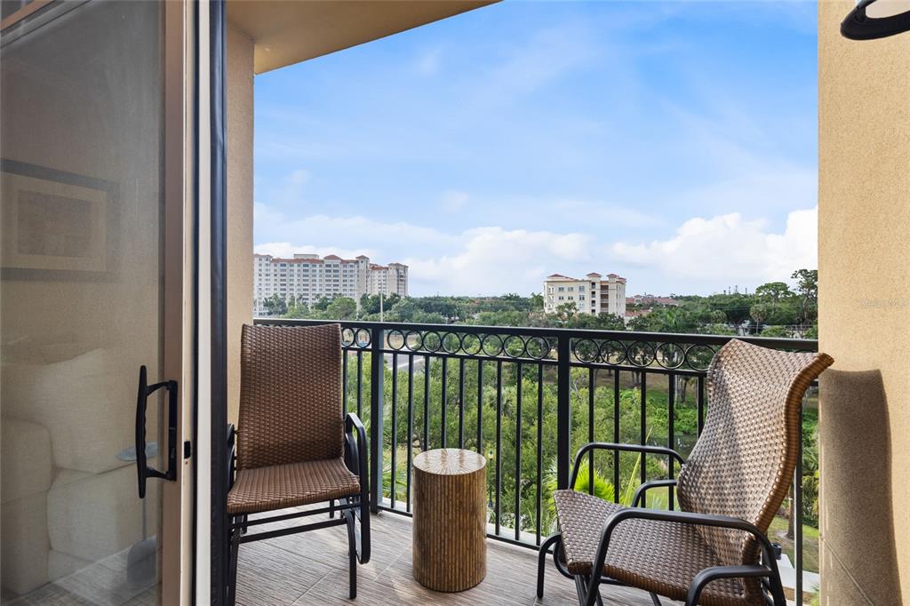 A balcony with two wicker chairs and a small table overlooks trees and distant buildings — 1064 N TAMIAMI TRAIL UNIT 1525, SARASOTA, FL
