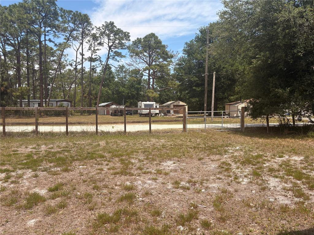 A fenced dirt lot features several small structures and trailers under a line of trees — 7810 W TWIN CANAL LANE, HOMOSASSA, FL