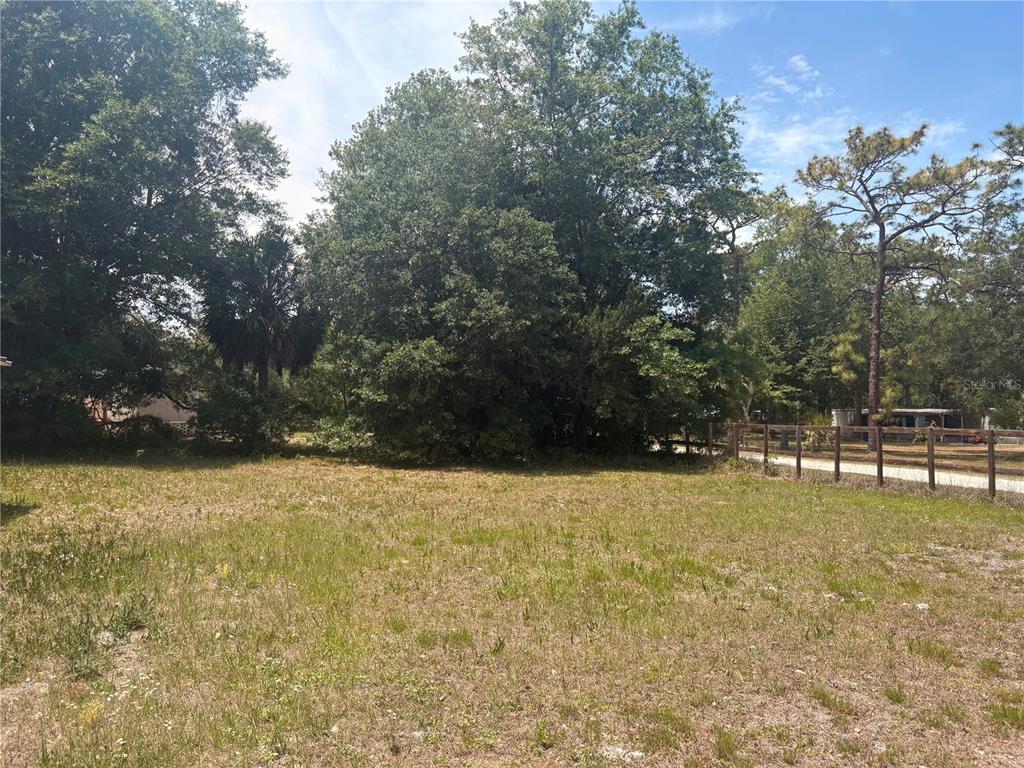 A grassy, vacant lot features mature trees and a wooden fence along the side — 7810 W TWIN CANAL LANE, HOMOSASSA, FL