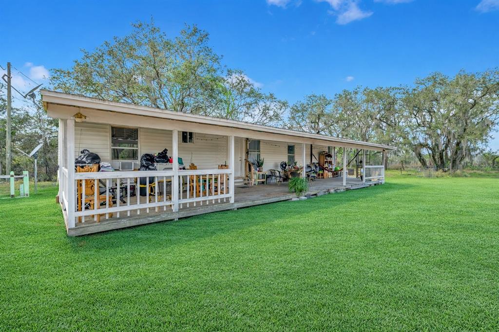 A long, single-story house with a wide, covered wooden porch and white siding — 5110 BAKER DAIRY ROAD, HAINES CITY, FL