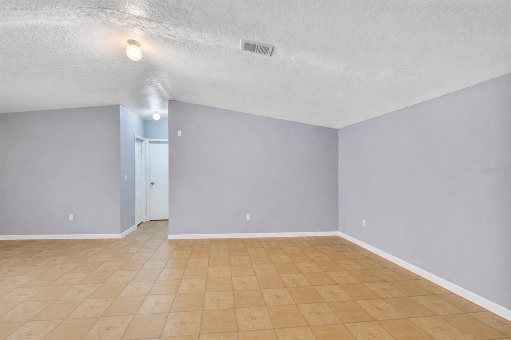 An empty room features light gray walls, a vaulted ceiling, and tan tile flooring — 5110 BAKER DAIRY ROAD, HAINES CITY, FL