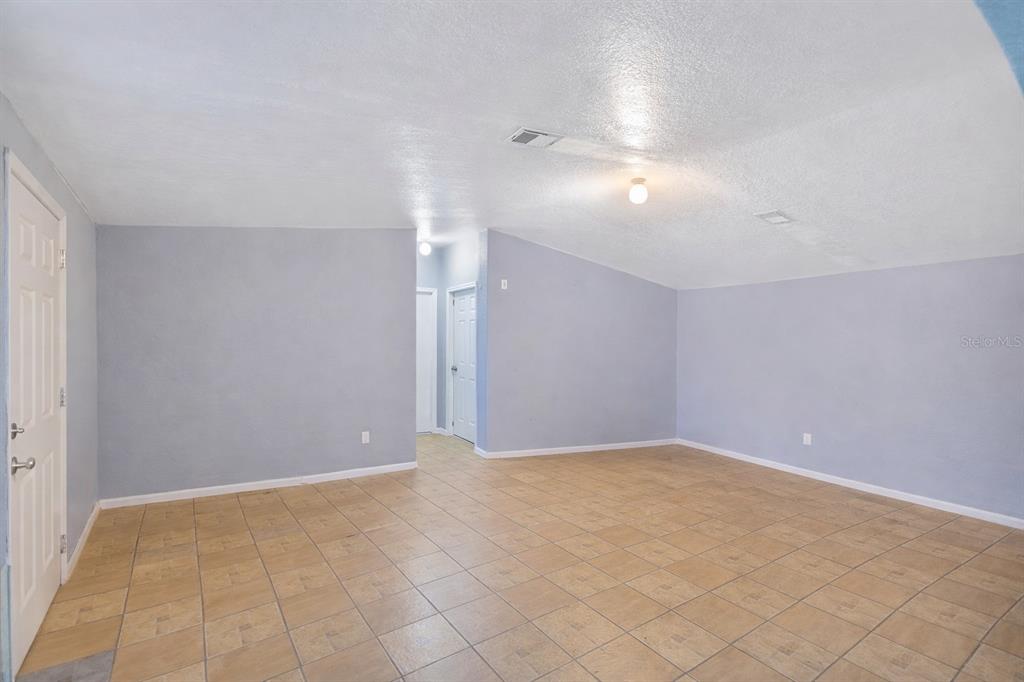 An empty room with light blue walls, tan tile flooring, and a vaulted ceiling — 5110 BAKER DAIRY ROAD, HAINES CITY, FL