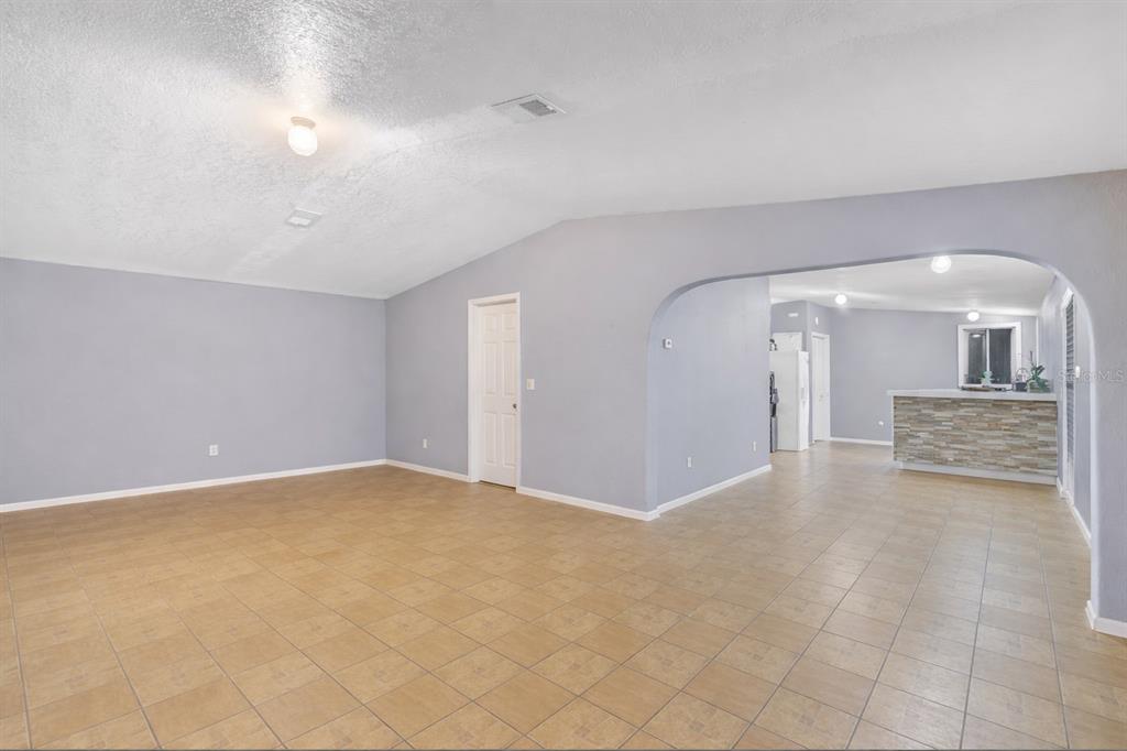 An open-concept living room features light gray walls, tan tile flooring, and an arched entryway — 5110 BAKER DAIRY ROAD, HAINES CITY, FL