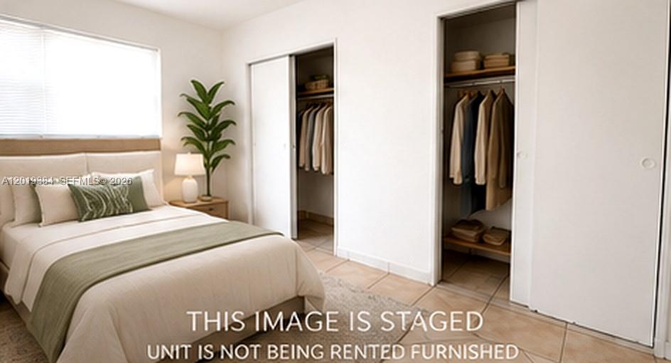 A staged bedroom features a bed, a potted plant, and two open closets with sliding doors — MIAMI BEACH, FL