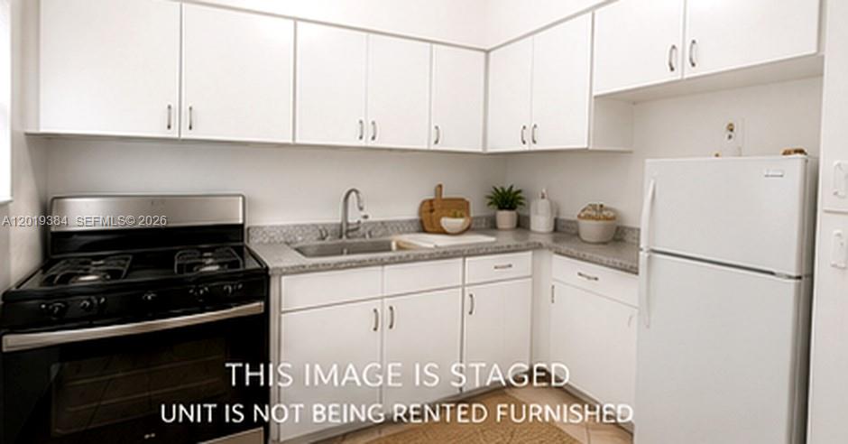 A kitchen features white cabinets, a black stove, a stainless steel sink, and a refrigerator — MIAMI BEACH, FL