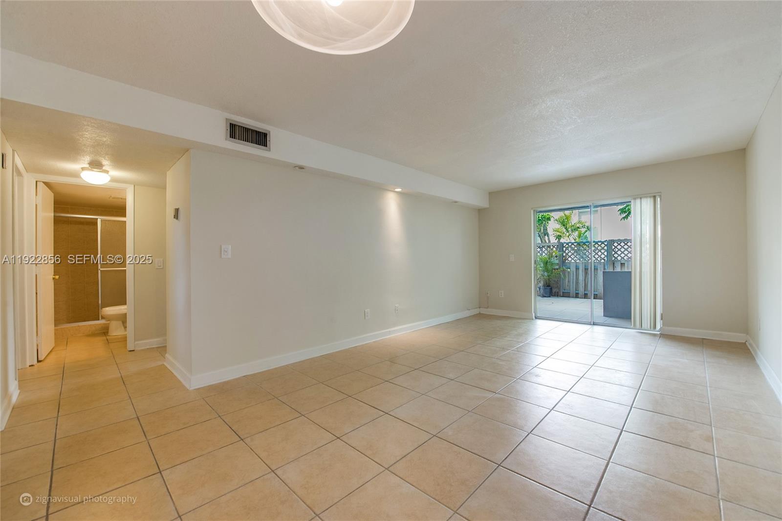 An empty room with beige tile flooring leads to a sliding glass door and patio — 4600 SW 67th Ave # 125, Miami FL 33155, MIAMI, FL