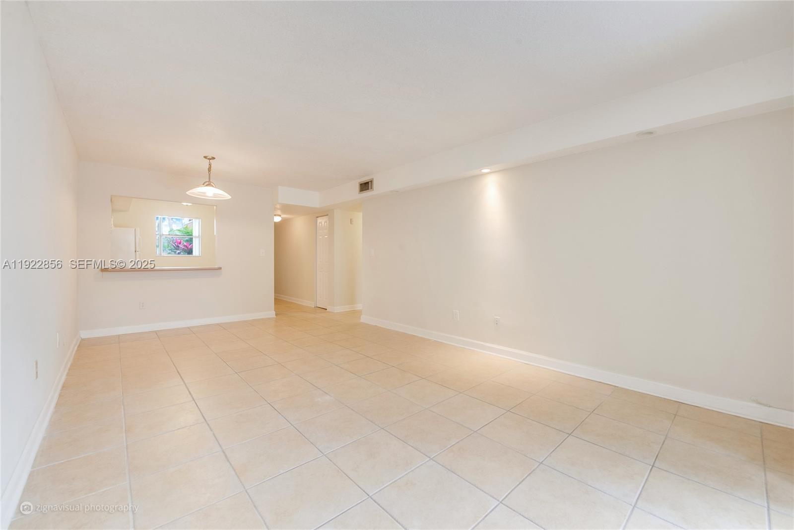 An empty room features light-colored tile flooring, white walls, and a pass-through kitchen window — 4600 SW 67th Ave # 125, Miami FL 33155, MIAMI, FL