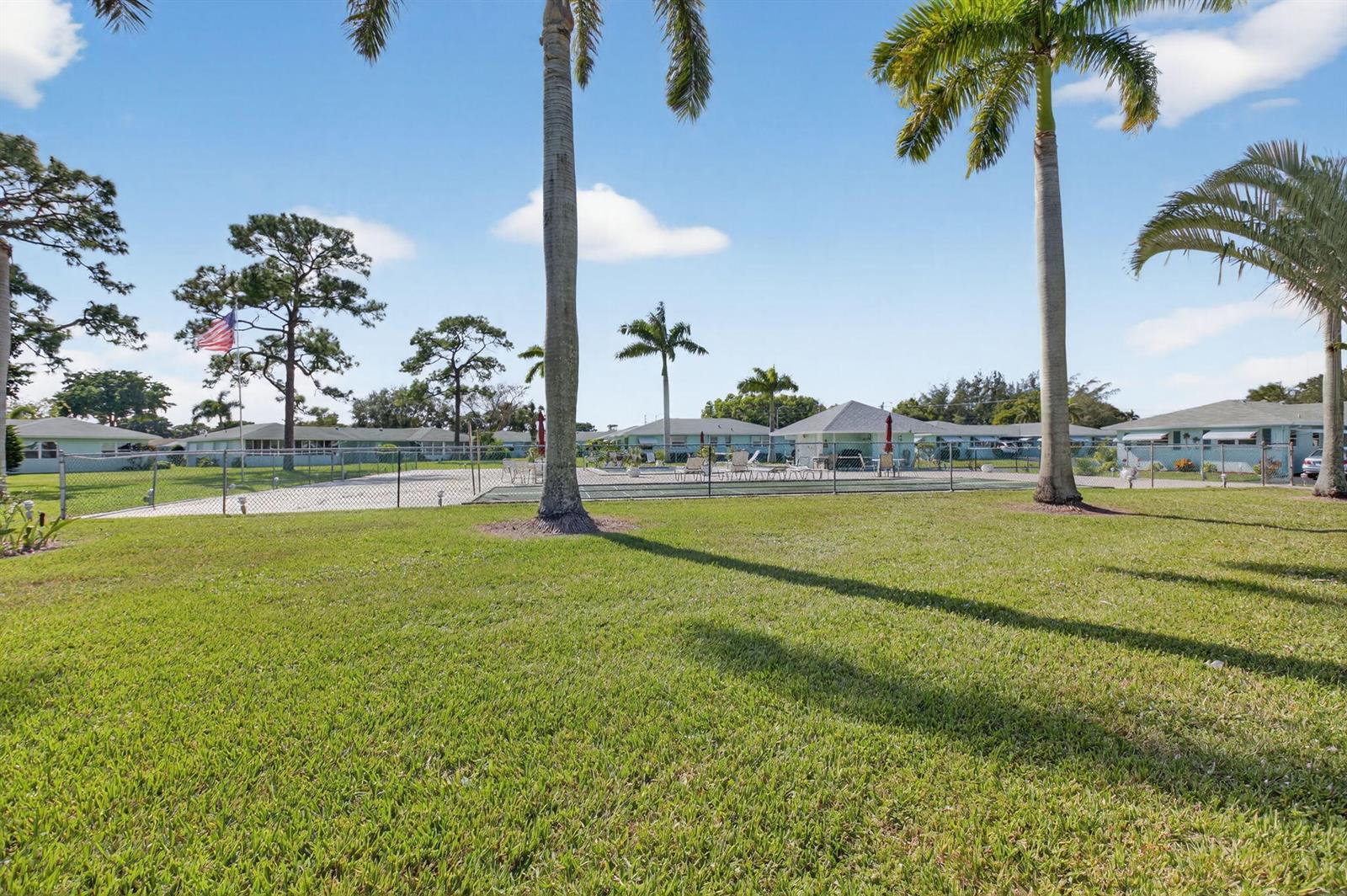 A grassy lawn with palm trees leads to a fenced pool area and residential buildings — 634 Hummingbird Lane, Delray Beach FL 33445, DELRAY BEACH, FL
