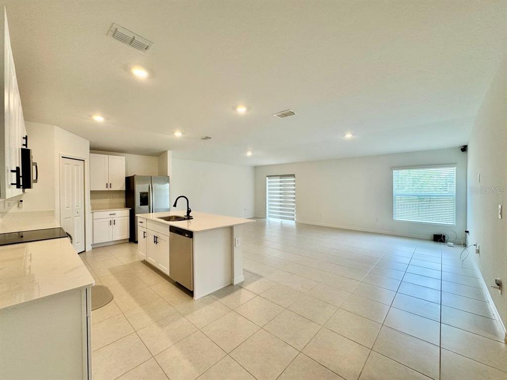 A bright, open-concept kitchen and living area with white cabinets, an island, and tile flooring — 10275 PURPLE LEAF COURT, RIVERVIEW, FL