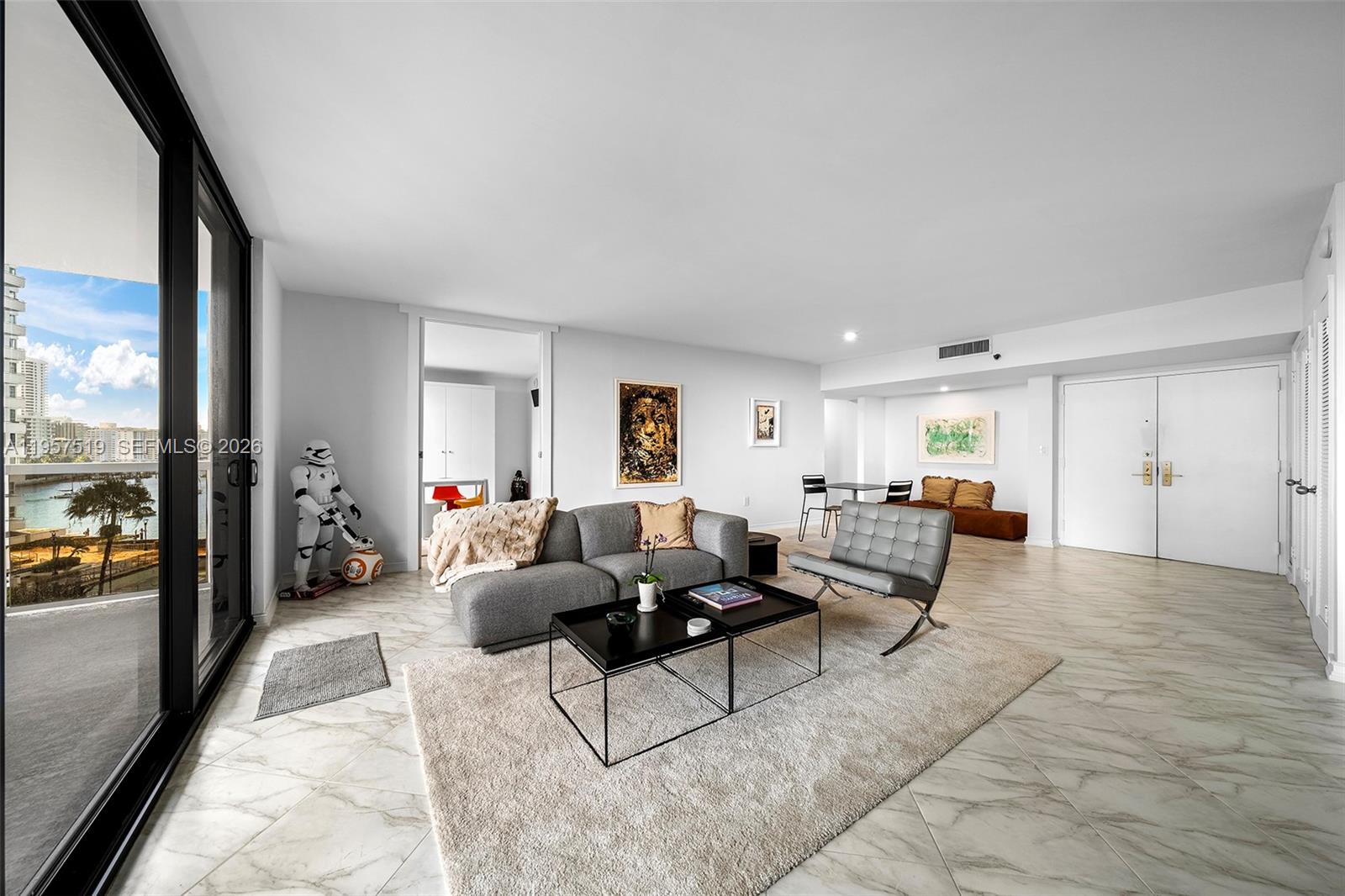 A modern living room features a grey sofa, a Barcelona chair, and a balcony view — 9 Island Ave # 710, Miami Beach FL 33139, MIAMI BEACH, FL