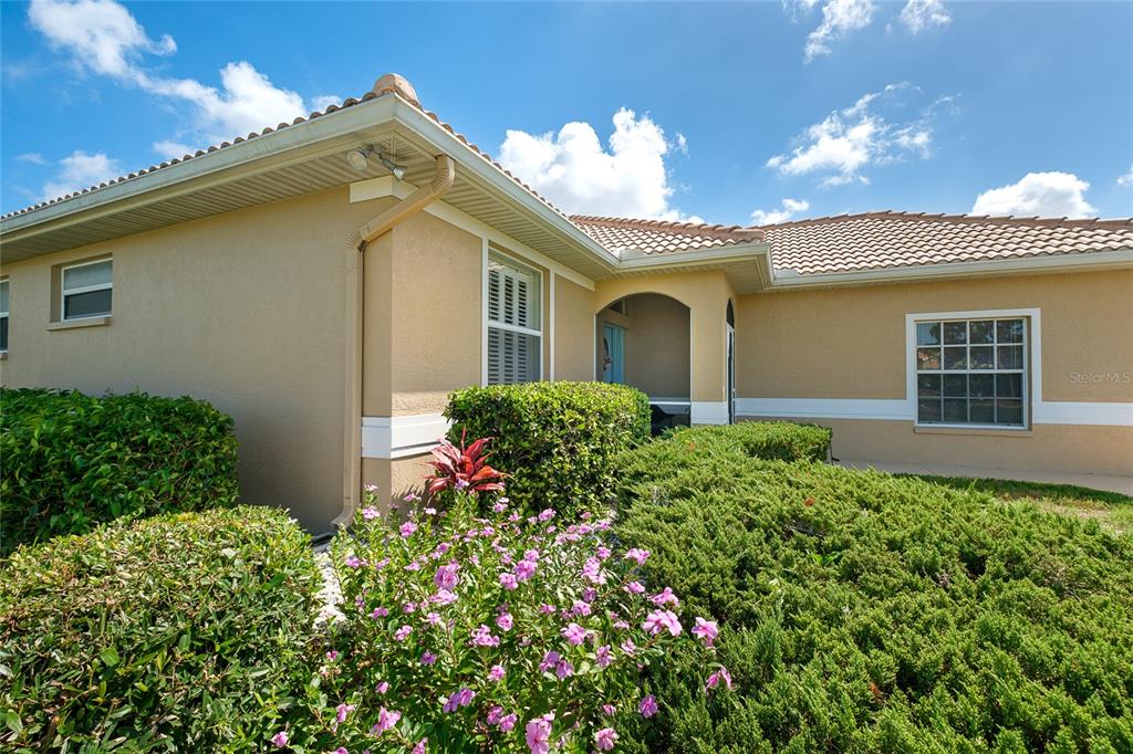 A tan house exterior features a tiled roof, green landscaping, and a covered front entryway — 6700 GREENVIEW LANE, ENGLEWOOD, FL