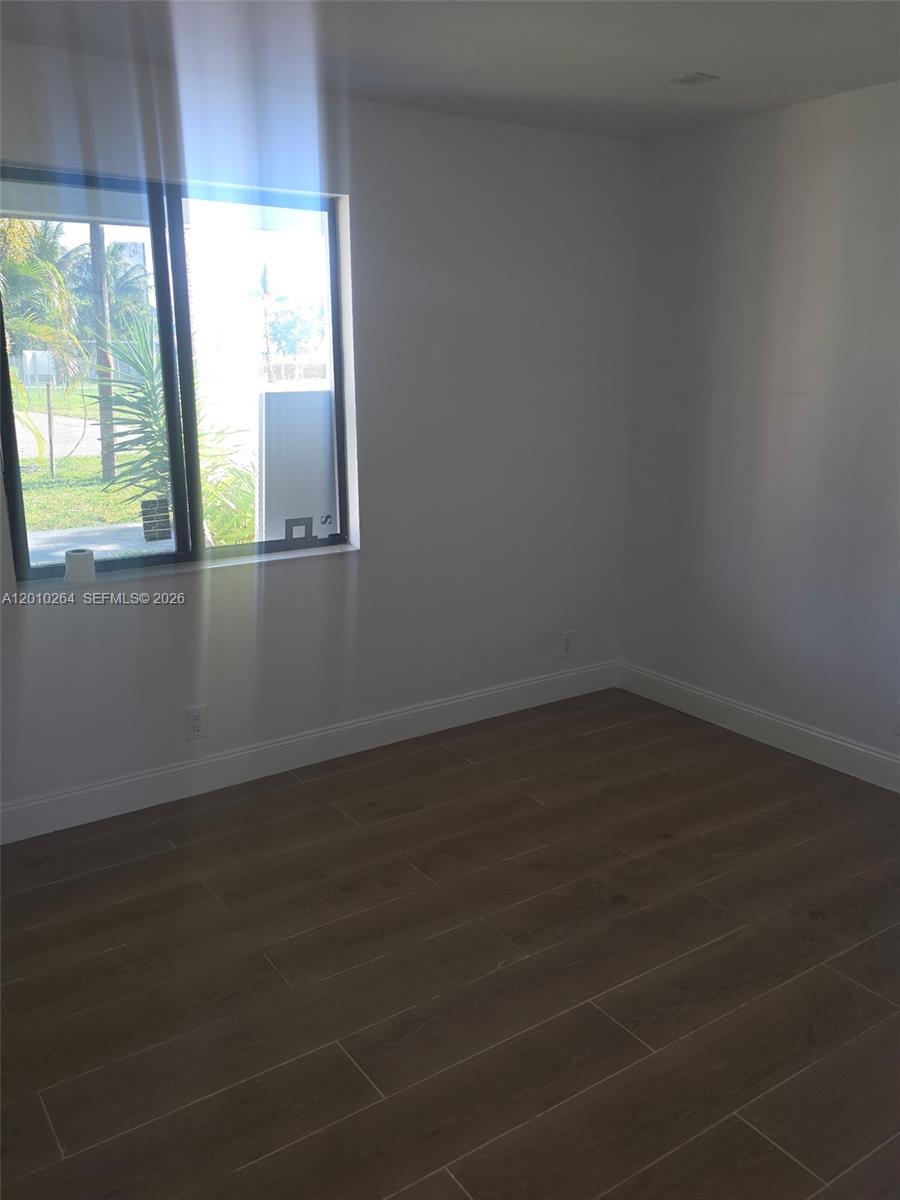An empty room features light gray walls, dark wood-look tile flooring, and a large window — 3300 SE 6th St # 2, Pompano Beach FL 33062, POMPANO BEACH, FL