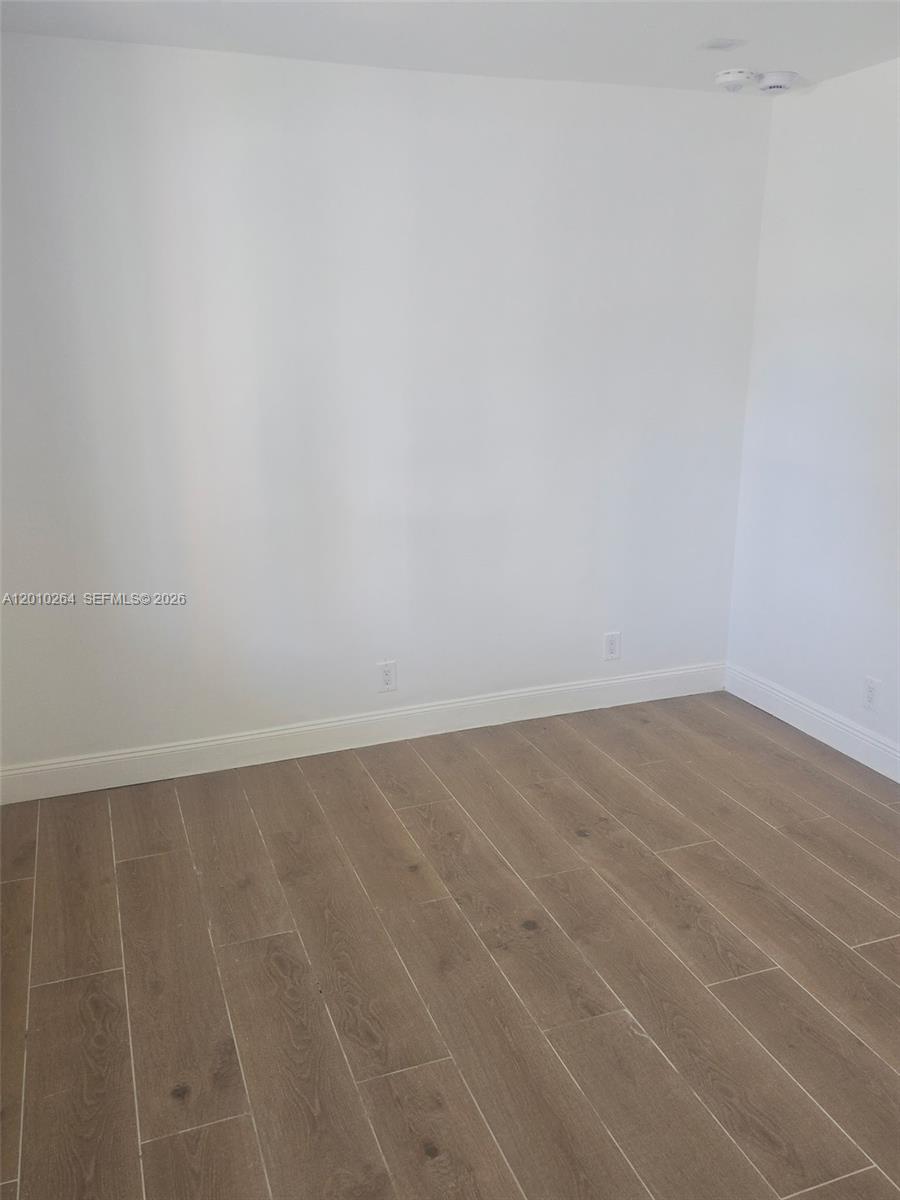An empty room features white walls, light wood-look flooring, and a ceiling-mounted smoke detector — 3300 SE 6th St # 2, Pompano Beach FL 33062, POMPANO BEACH, FL