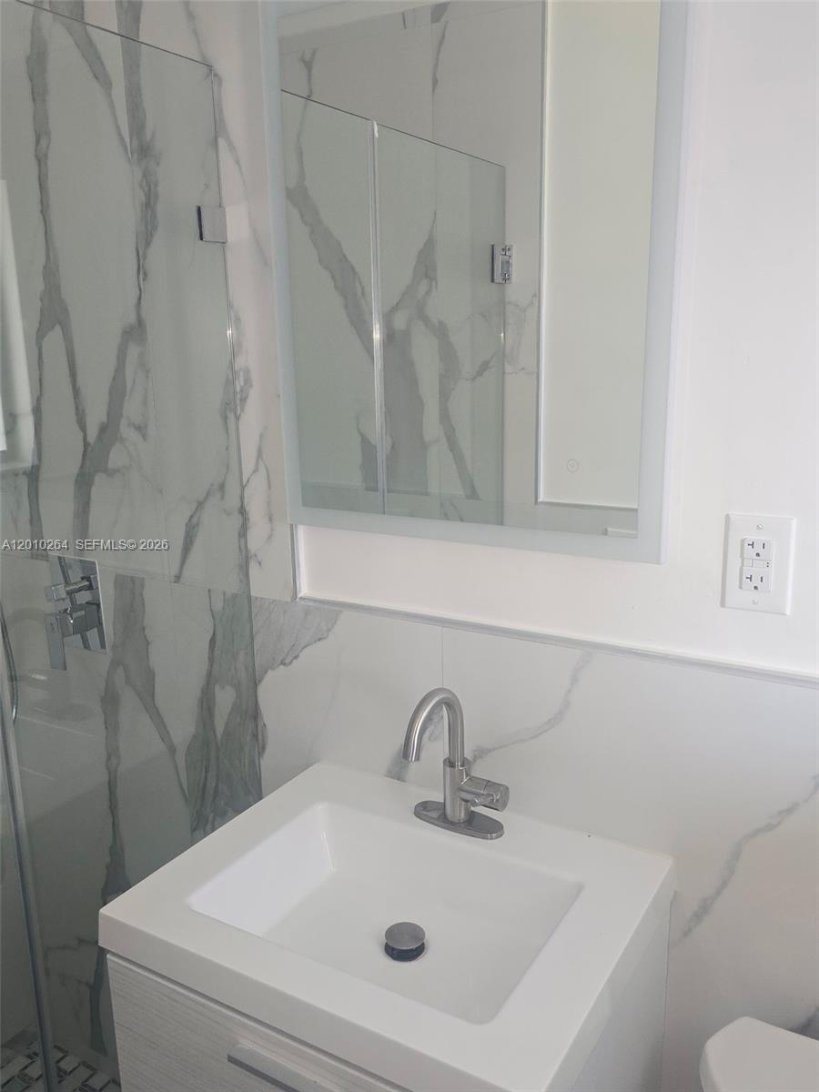 A modern bathroom features a white vanity, marble-patterned wall tiles, and a glass shower enclosure — 3300 SE 6th St # 2, Pompano Beach FL 33062, POMPANO BEACH, FL