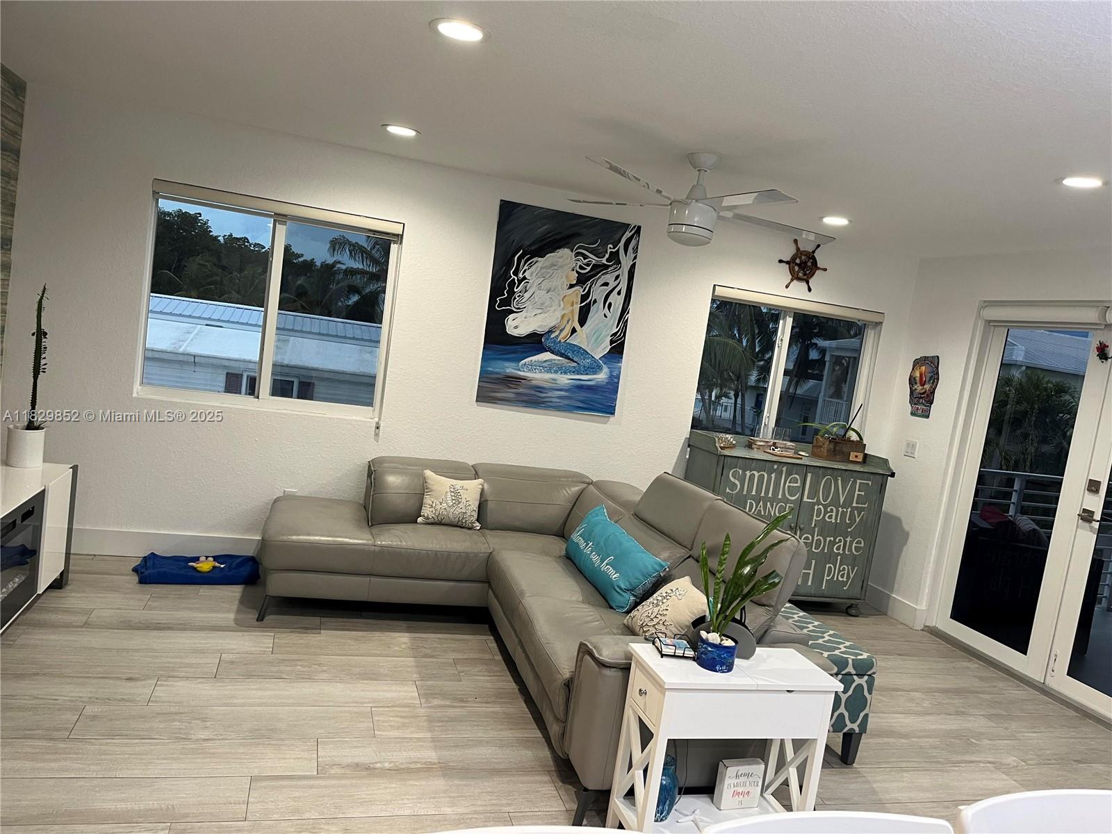 A living room features a grey sectional sofa, mermaid wall art, and light wood-look flooring — 325 Calusa St 96, Key Largo FL 33037, KEY LARGO, FL