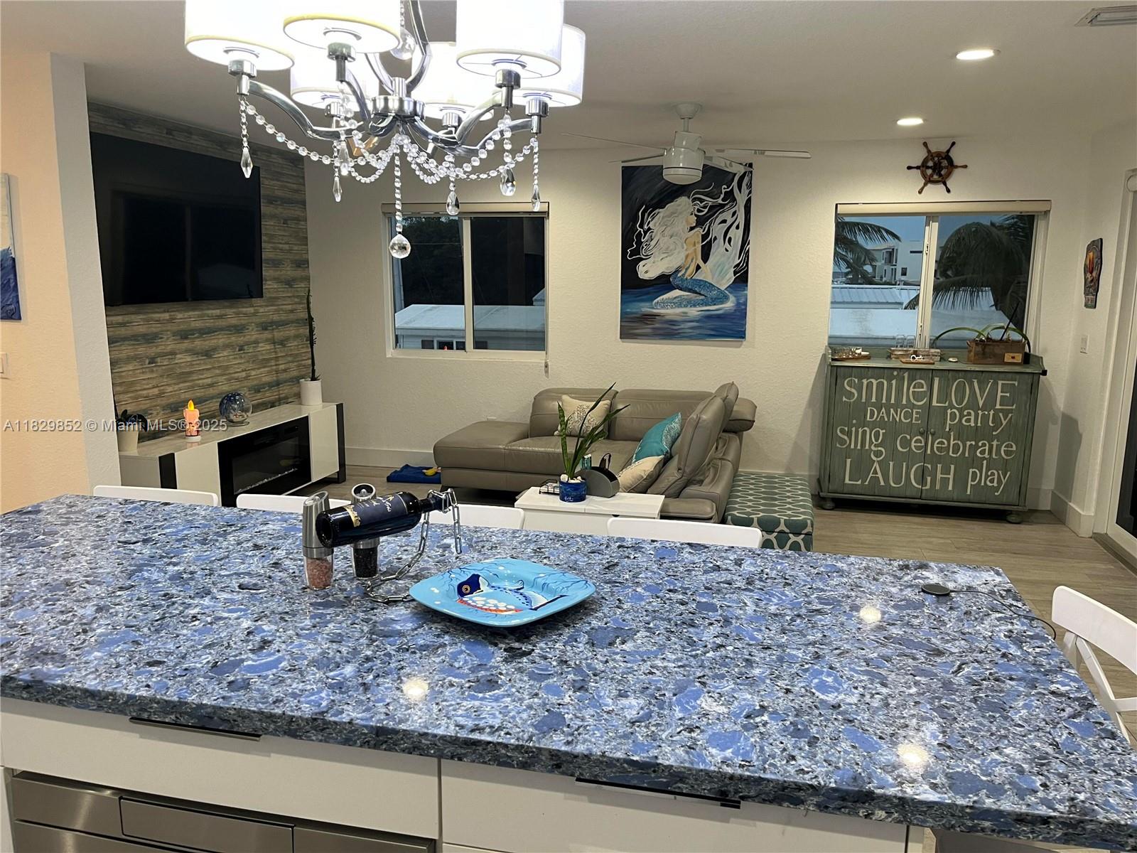 A kitchen island with a blue speckled countertop overlooks a living room with coastal decor — 325 Calusa St 96, Key Largo FL 33037, KEY LARGO, FL