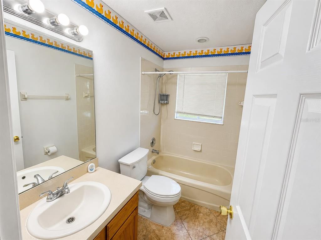 A bathroom features a vanity, toilet, and a bathtub with a shower head and window — 320 PARADISE WOODS PLACE, DAVENPORT, FL
