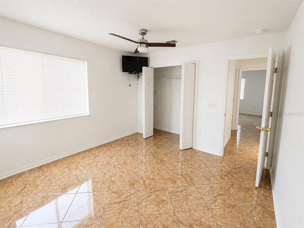 An empty bedroom features tan tile flooring, a ceiling fan, and a walk-in closet — 320 PARADISE WOODS PLACE, DAVENPORT, FL