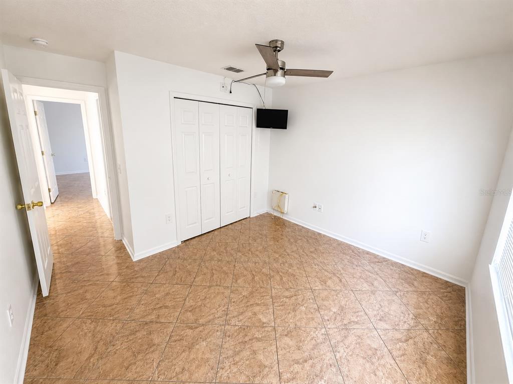 An empty bedroom features white walls, tile flooring, a ceiling fan, and a closet — 320 PARADISE WOODS PLACE, DAVENPORT, FL