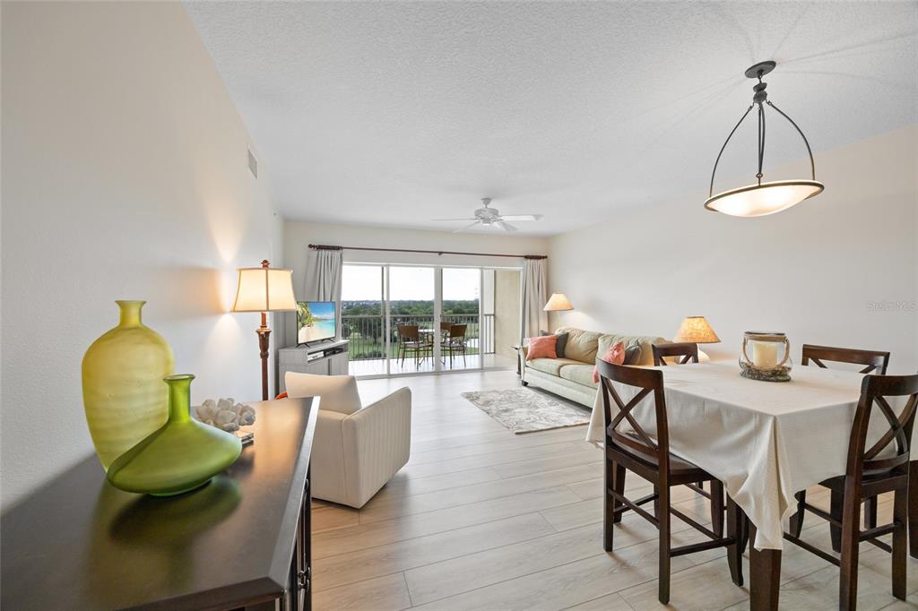 A bright living and dining area features light wood floors, a balcony, and neutral furniture — 1200 COUNTRY CLUB DRIVE UNIT 5402, LARGO, FL