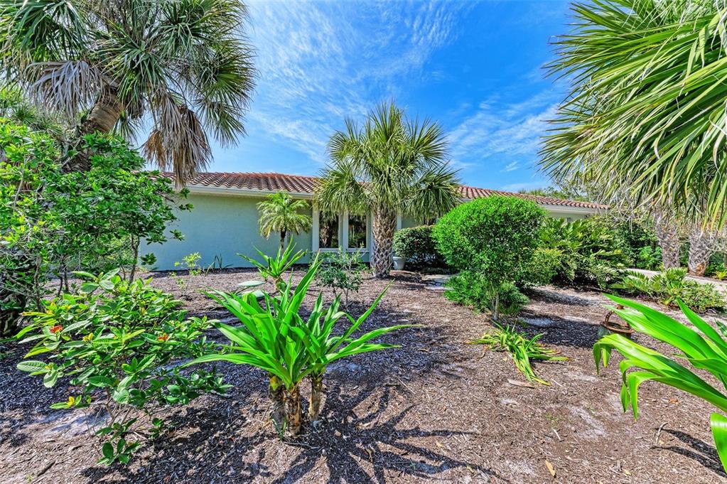 A view of a house exterior with a tiled roof, palm trees, and landscaped yard — 8320 MANASOTA KEY ROAD, ENGLEWOOD, FL