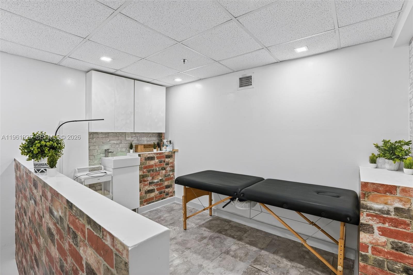 A treatment room features a massage table, a small sink, and brick accent walls — 8750 W Flagler St # 2, Miami FL 33174, MIAMI, FL