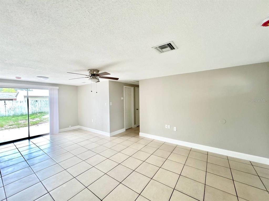 An empty room features beige tile flooring, a ceiling fan, and sliding glass patio doors — 3323 FAIRMOUNT DRIVE, HOLIDAY, FL