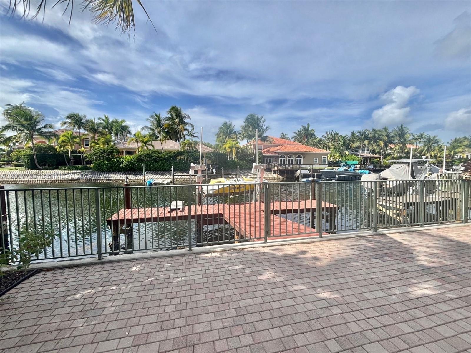 A view of a canal with a wooden dock, boats, and houses under a cloudy sky — 1141 Waterside Ln, Hollywood FL 33019, HOLLYWOOD, FL