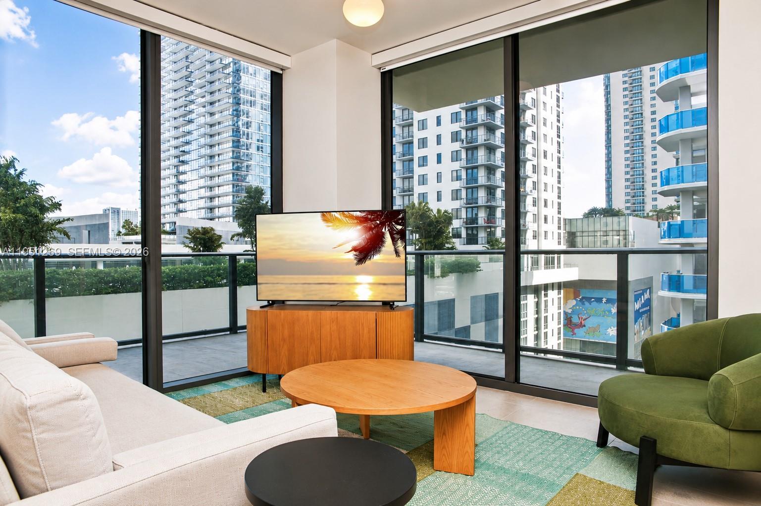A living room features floor-to-ceiling windows, a television on a wooden console, and city views — 11 NE 6th St # 1109, Miami FL 33132, MIAMI, FL