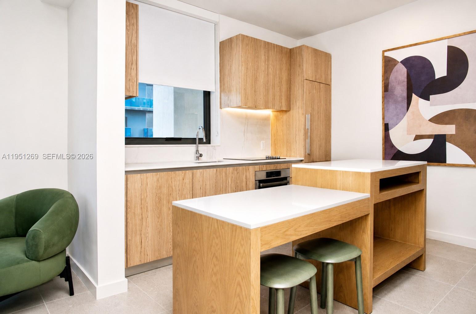 A modern kitchen features light wood cabinetry, white countertops, and a matching island with stools — 11 NE 6th St # 1109, Miami FL 33132, MIAMI, FL