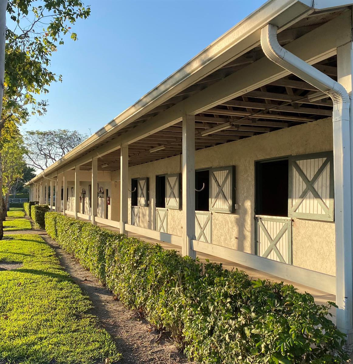 A long, single-story horse stable with a covered walkway and green-trimmed stall doors — 5110 S Shore Boulevard, Wellington FL 33449, WELLINGTON, FL