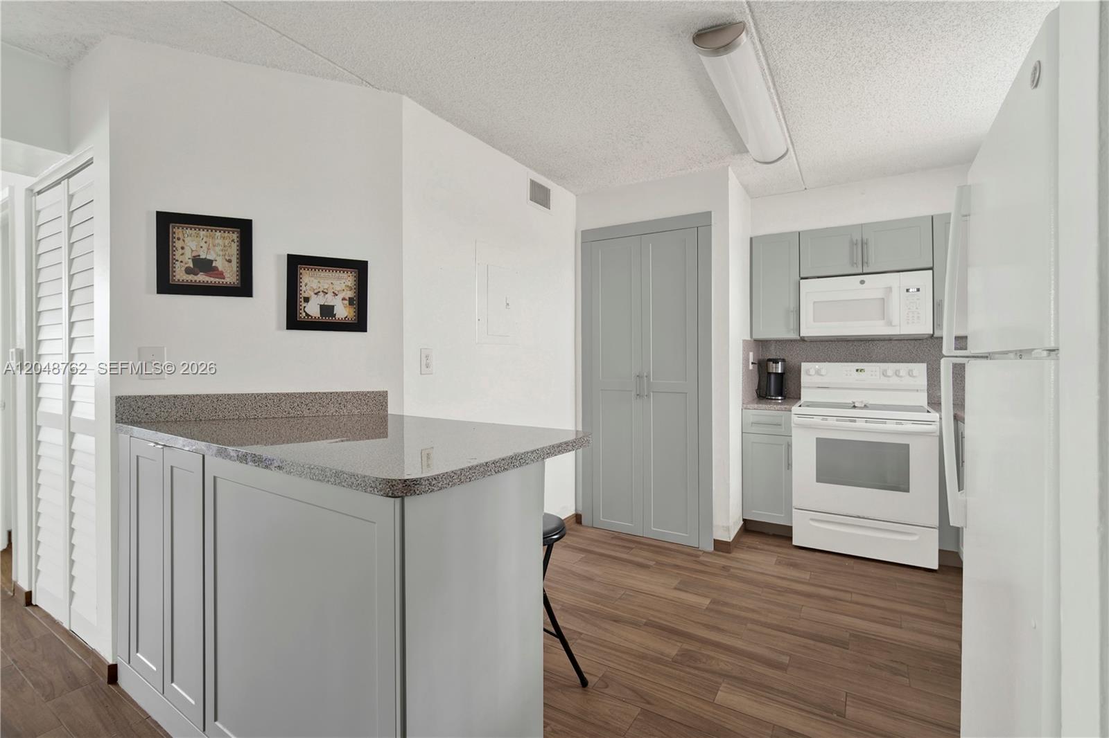 A kitchen features gray cabinets, a granite-topped island, white appliances, and wood-look flooring — HIALEAH, FL