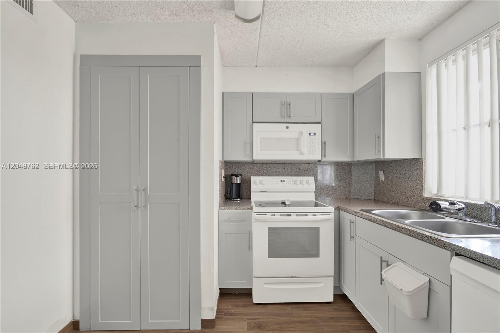 A kitchen features grey cabinets, white appliances, a speckled countertop, and wood-look flooring — HIALEAH, FL