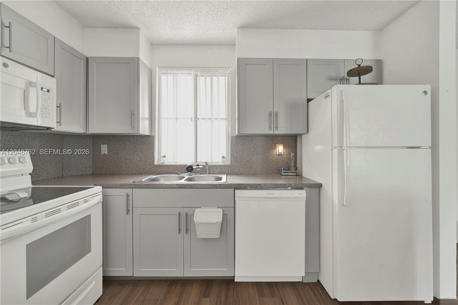 A kitchen features grey cabinets, white appliances, a window above the sink, and speckled countertops — HIALEAH, FL