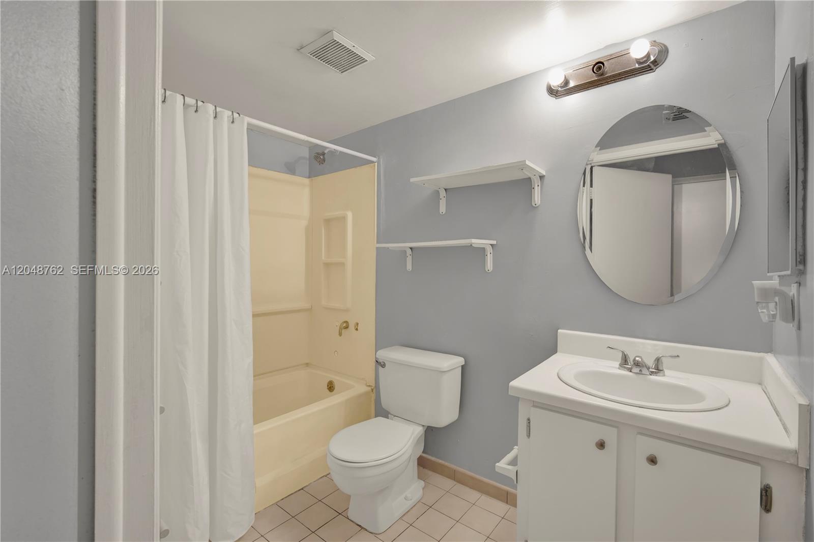 A bathroom features a beige tub-shower combo, a white toilet, and a vanity with a mirror — HIALEAH, FL
