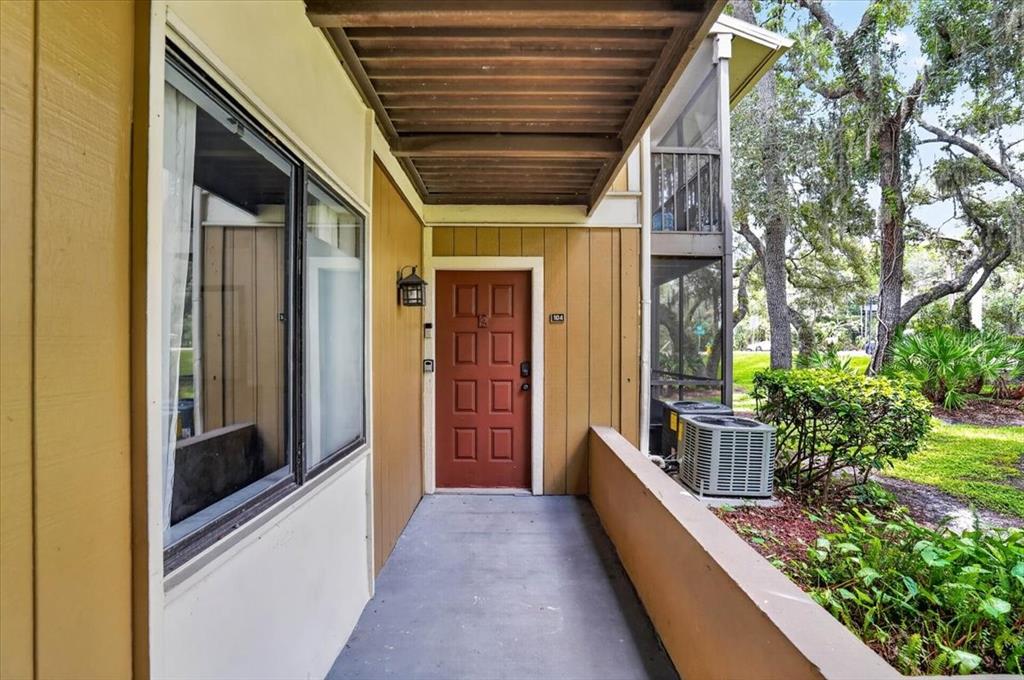 A covered walkway leads to the red front door of a tan-sided apartment building — 13405 ARBOR POINTE CIRCLE UNIT 104, TAMPA, FL