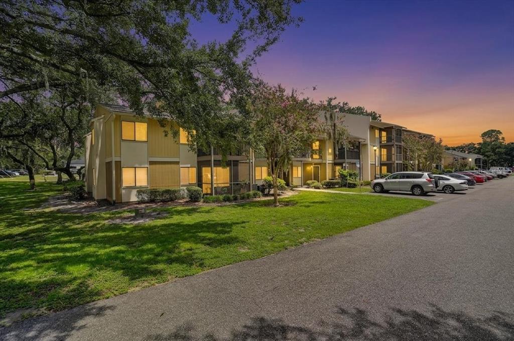 A two-story apartment building with yellow siding stands next to a parking lot at sunset — 13405 ARBOR POINTE CIRCLE UNIT 104, TAMPA, FL