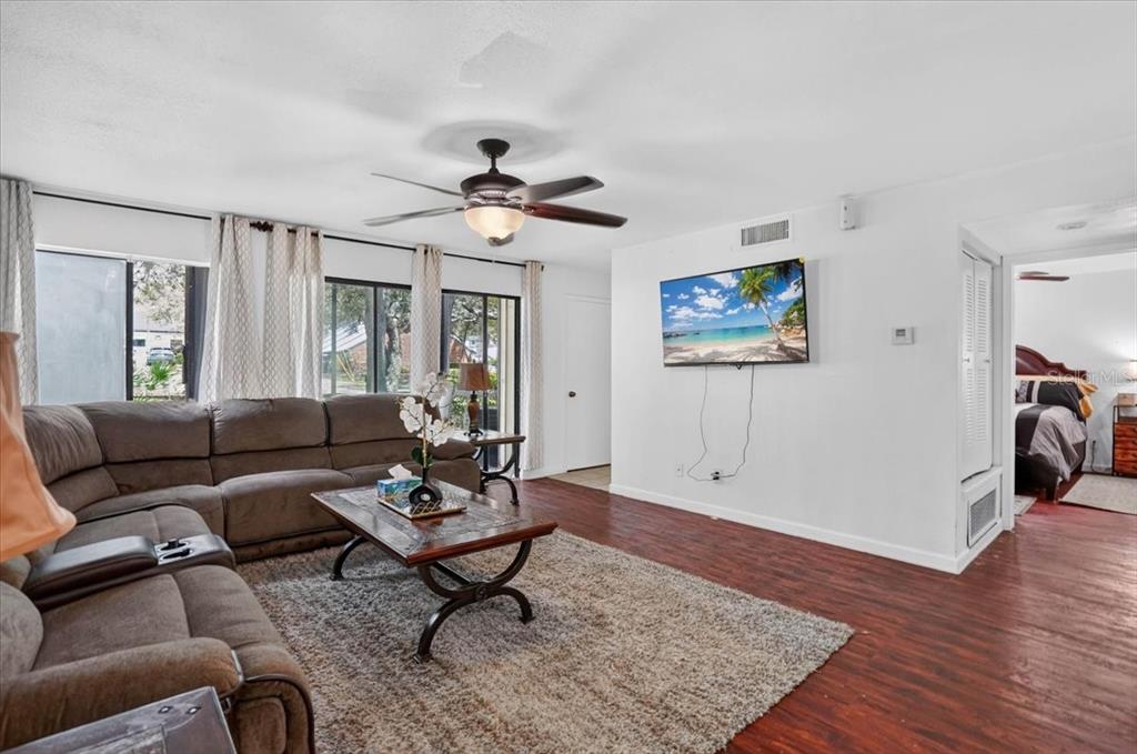 A living room with a brown sectional sofa, coffee table, ceiling fan, and wall-mounted television — 13405 ARBOR POINTE CIRCLE UNIT 104, TAMPA, FL