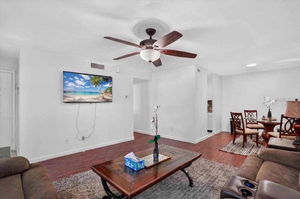 A living room with wood-look flooring, a ceiling fan, and a wall-mounted television — 13405 ARBOR POINTE CIRCLE UNIT 104, TAMPA, FL