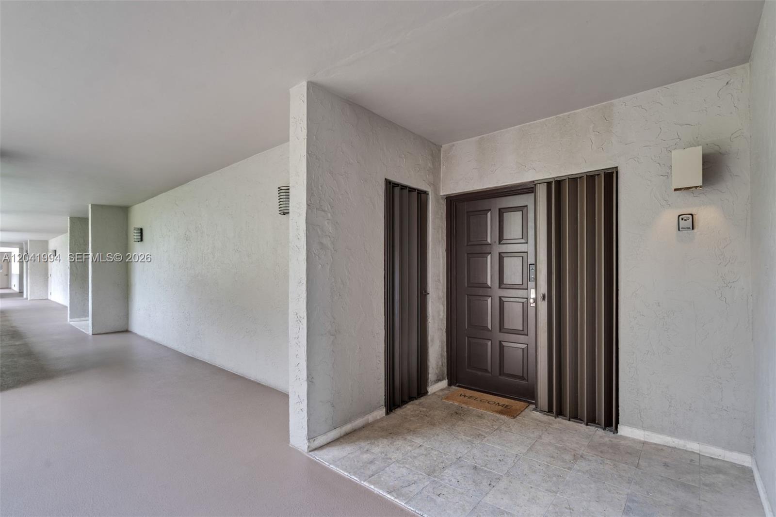 A brown front door with accordion shutters is situated in a covered outdoor hallway — 101 Crandon Blvd # 269, Key Biscayne FL 33149, KEY BISCAYNE, FL
