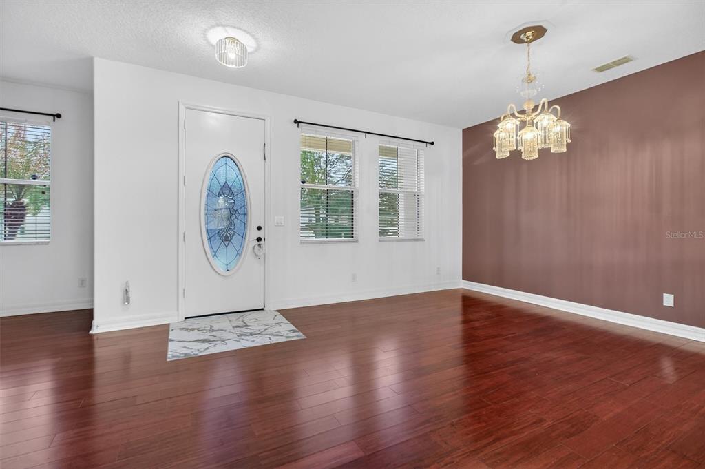 A dining room features dark wood flooring, a brown accent wall, and a crystal chandelier — 3106 ANQUILLA AVENUE, CLERMONT, FL