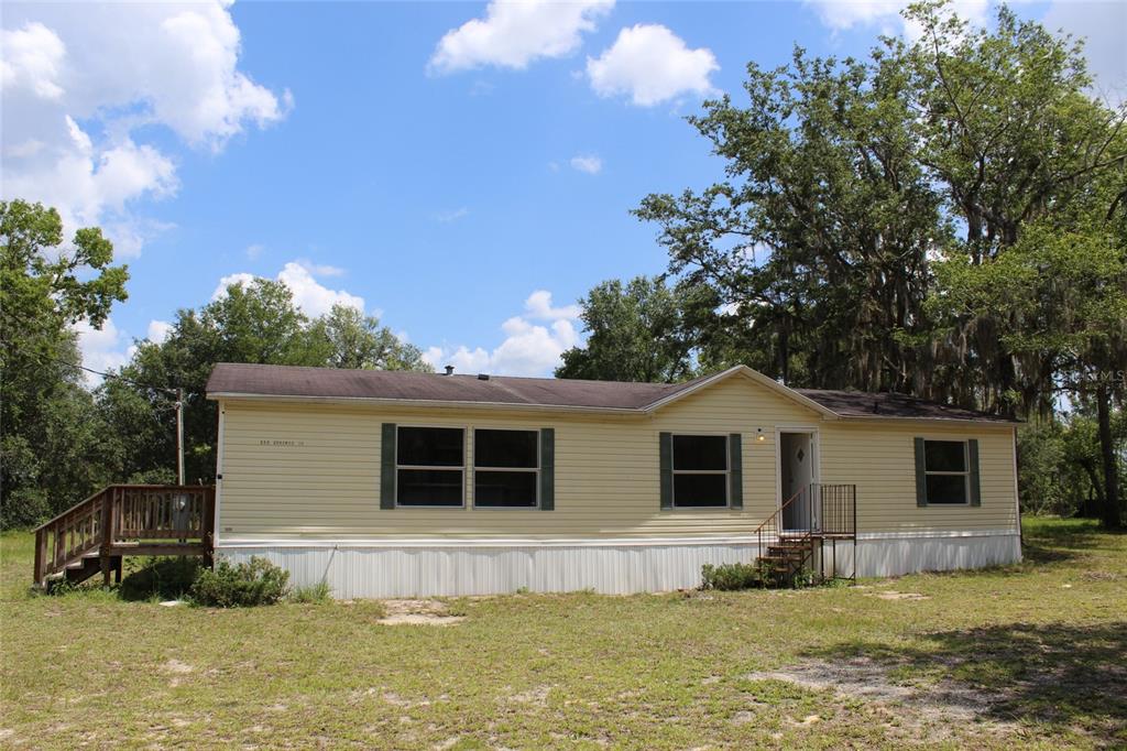 A single-story yellow manufactured home with a wooden deck and metal stairs sits outdoors — 112 JUNIPER DRIVE, HAWTHORNE, FL