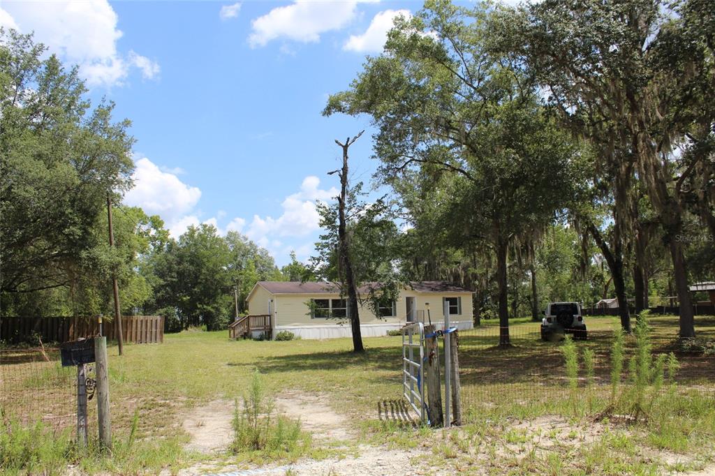 A single-story house with yellow siding sits on a grassy lot with mature trees — 112 JUNIPER DRIVE, HAWTHORNE, FL